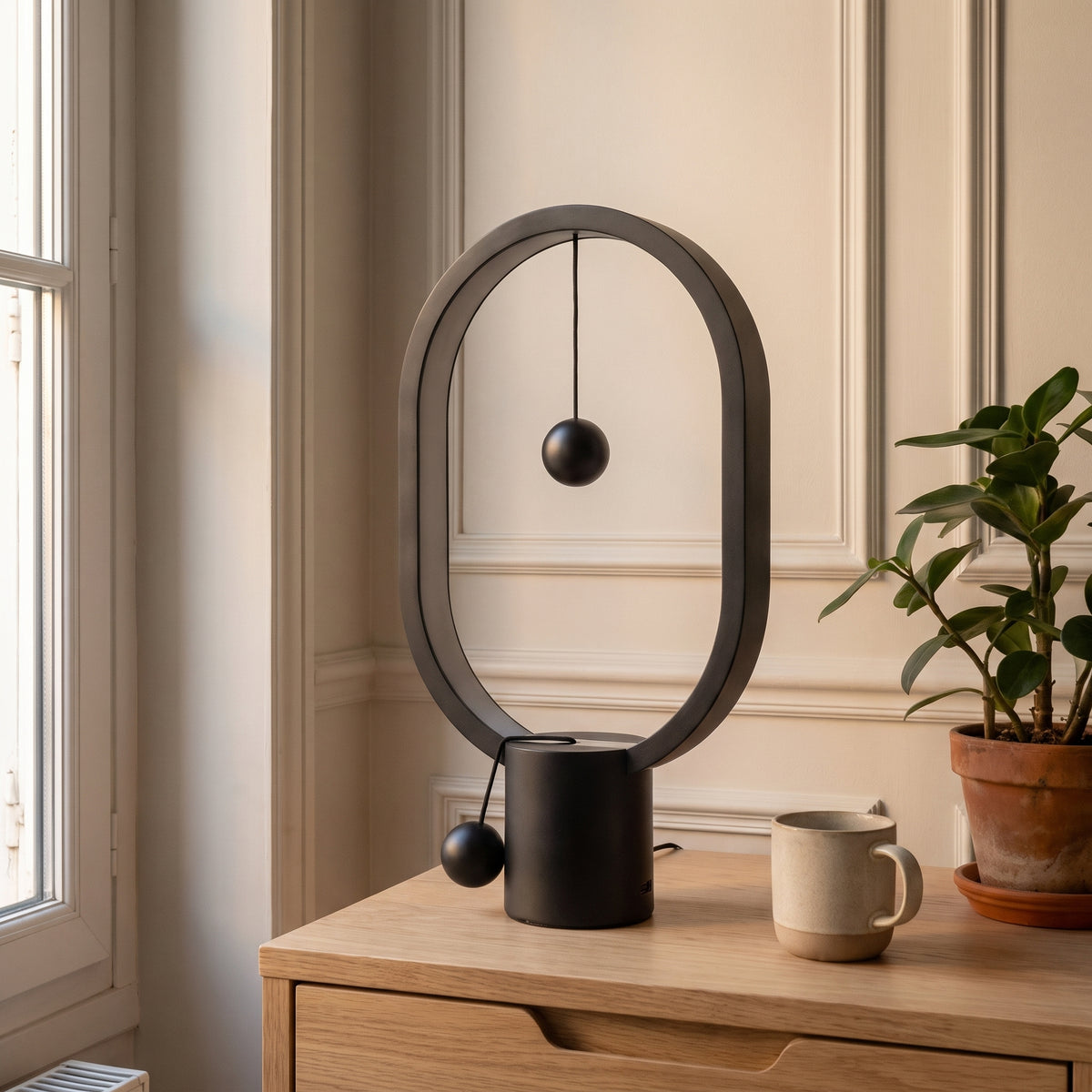 Lampe de chevet ovale en métal noir à billes magnétiques, éteinte, les billes séparées, sur une table de chevet