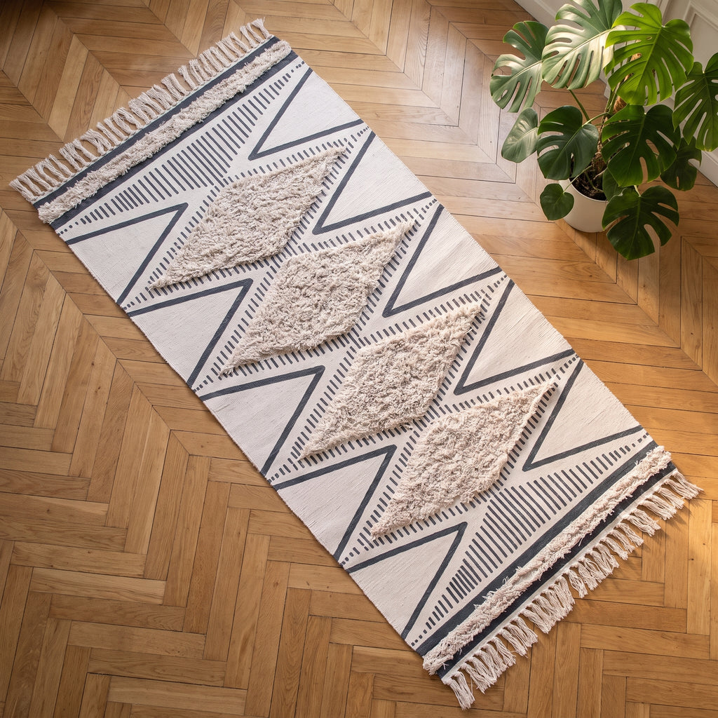Le tapis ethnique vu du dessus, entier, ses losanges tuftés et ses franges sur un parquet à chevrons