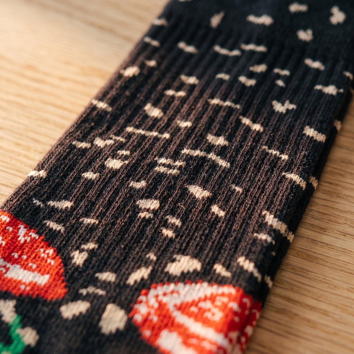 Gros plan sur la maille d’une tige : les côtes verticales du tricot de coton, les éclats beiges semés sur le fond brun sombre et le bord d’une tranche rouge marbrée de blanc