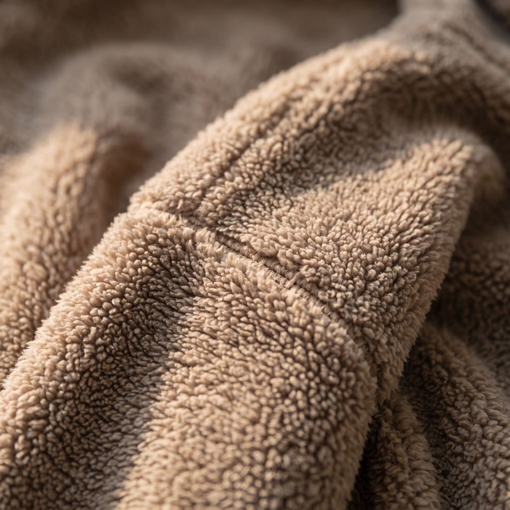 Gros plan sur l epaule du sweat marron en lumiere rasante : la couture d epaule traverse le cadre et chaque boucle du tissu porte son ombre