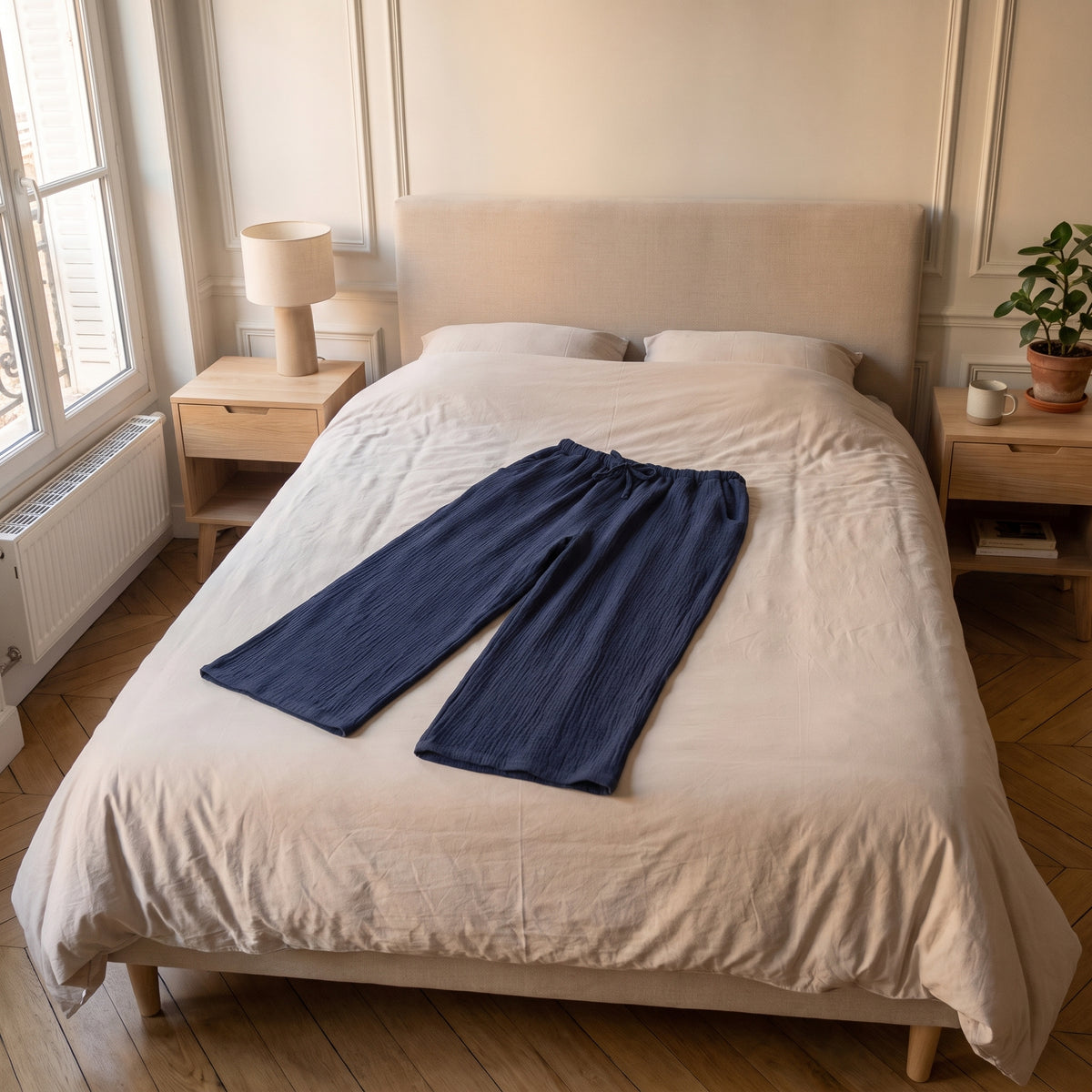 Pantalon d'intérieur bleu marine en gaze de coton posé à plat sur le lit fait de la chambre, vu depuis le pied du lit