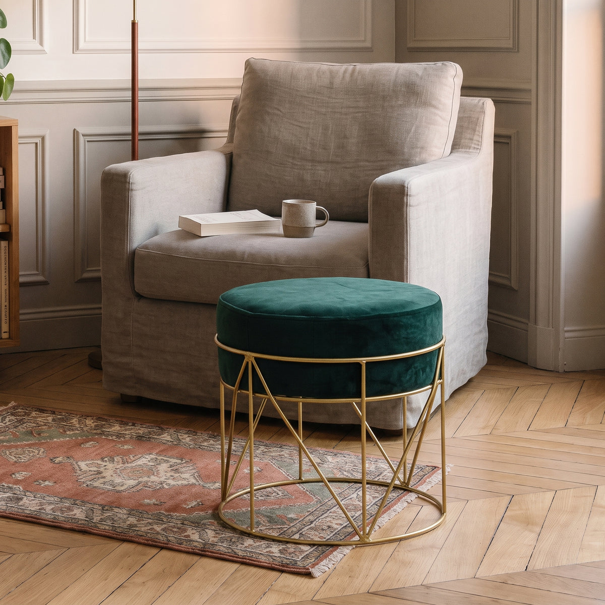 Pouf en velours vert sapin posé en repose-pieds devant un fauteuil de lecture