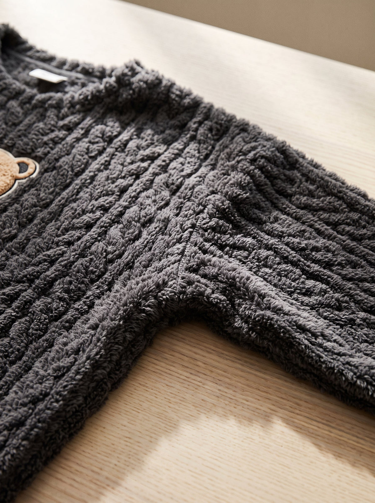 Gros plan de l epaule et de la manche du pyjama anthracite : torsades gaufrees de la maille polaire.