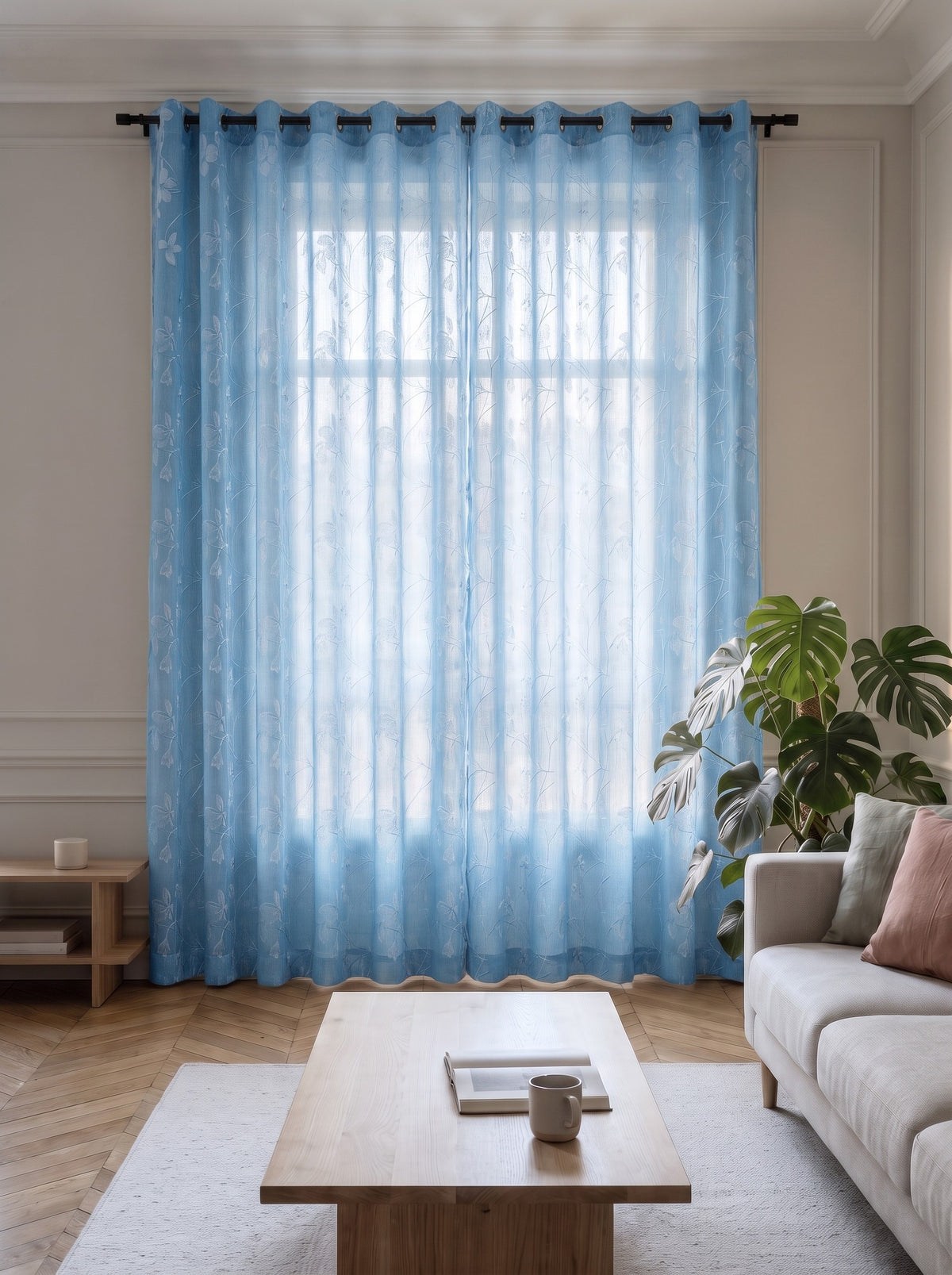 Voilage transparent bleu à motif feuillage, pans fermés devant la fenêtre d'un salon
