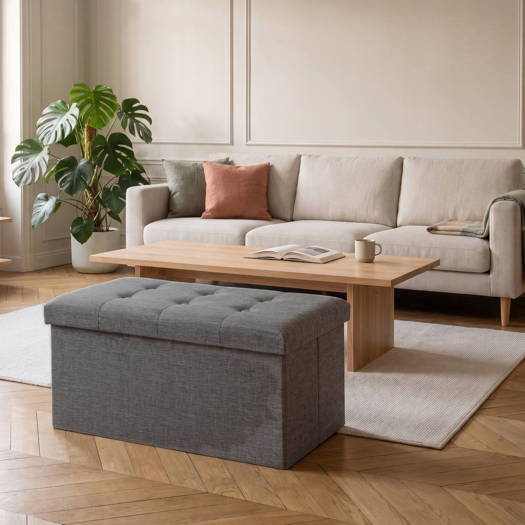 Tabouret coffre de rangement pliable gris foncé devant une table basse en bois clair
