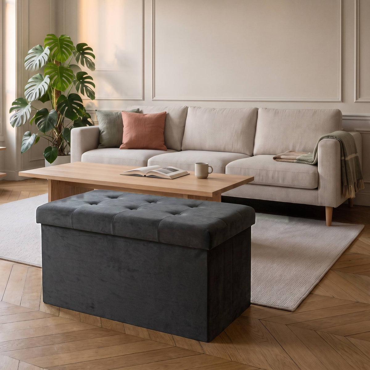 Tabouret coffre de rangement pliable en velours gris devant un canapé écru