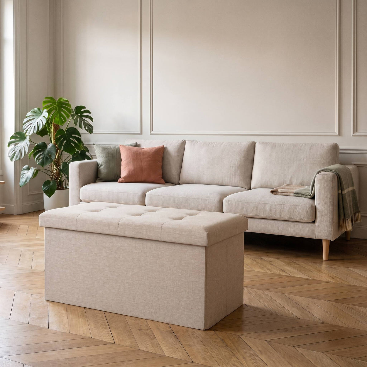 Tabouret coffre de rangement pliable crème devant un canapé écru