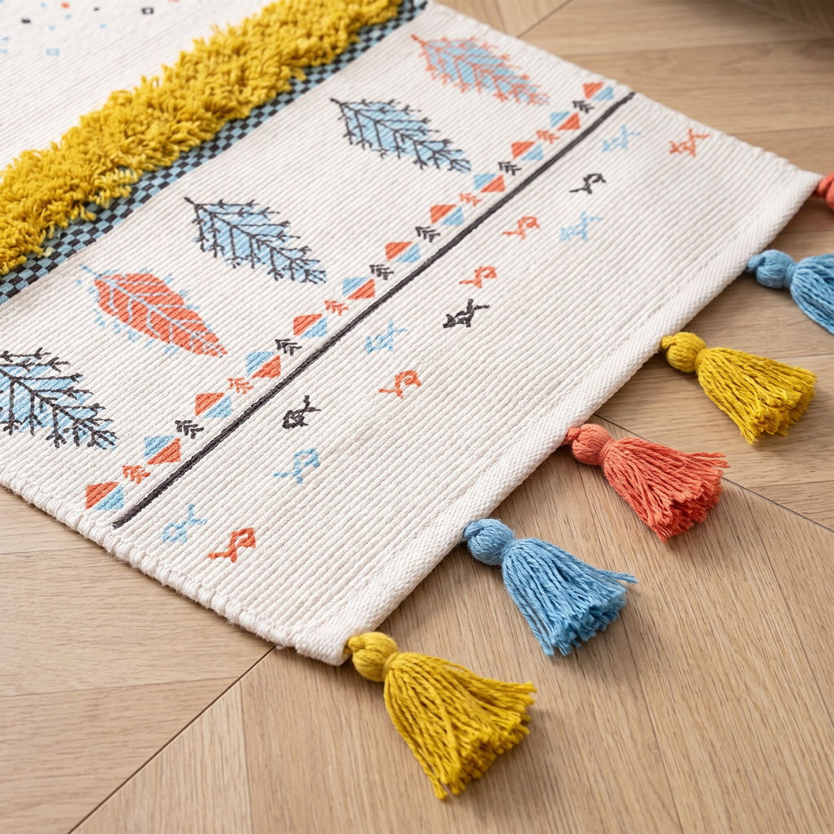 Pompons noués jaune moutarde, corail et bleu ciel au bord du petit tapis