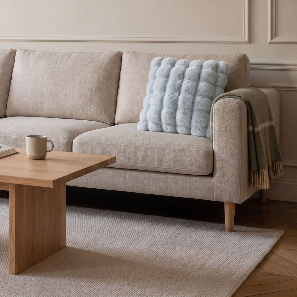 Coussin carré en fausse fourrure bleue posé sur le canapé d'un salon clair