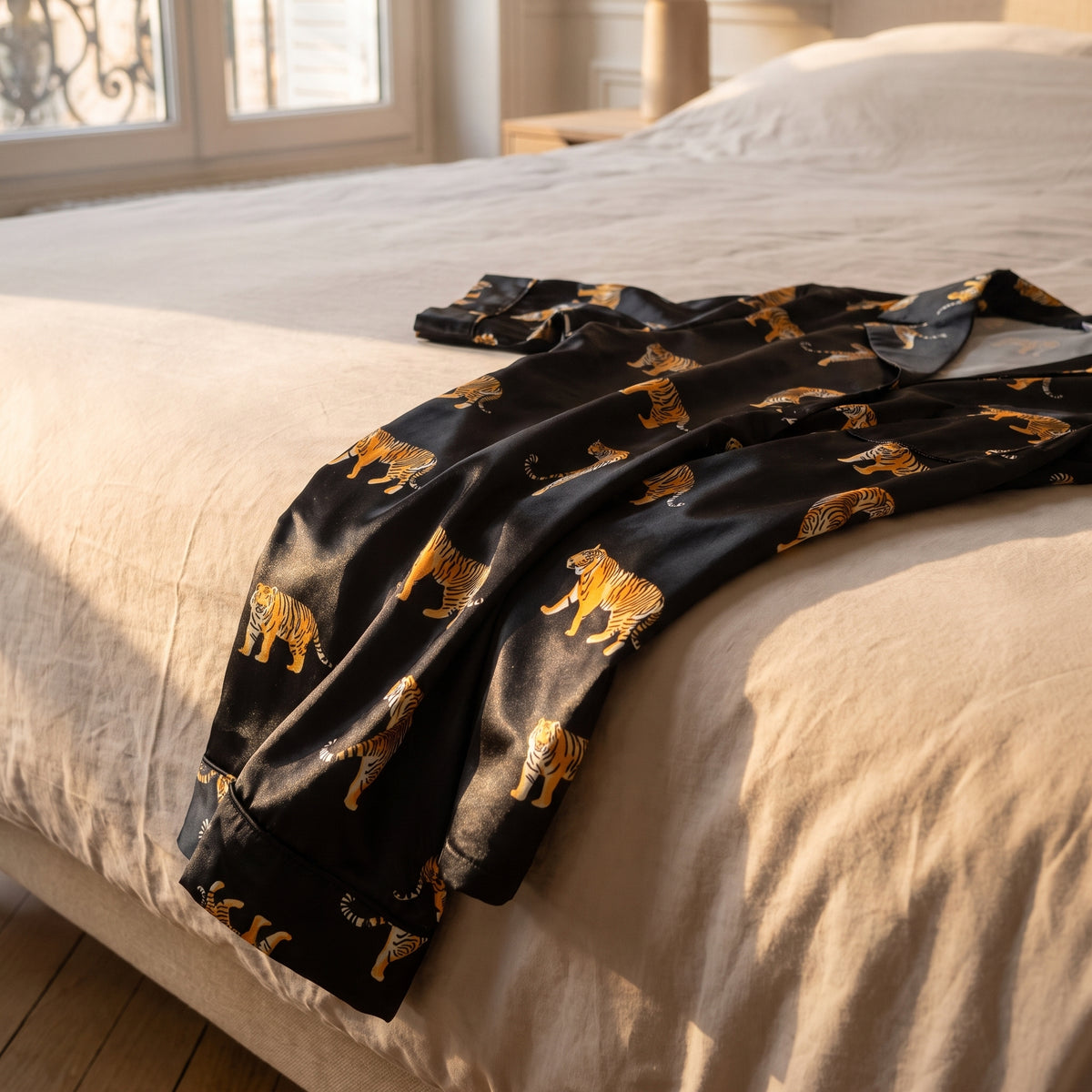Satin noir du pyjama drapé sur le bord du lit, tigres orange de l'imprimé vus de près
