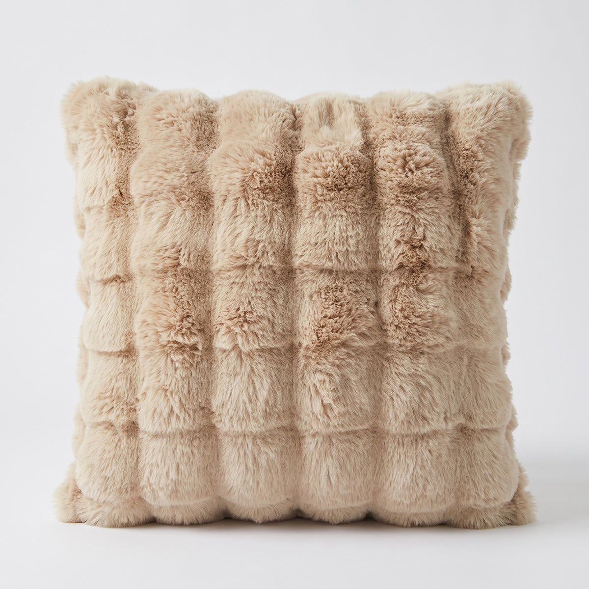 Coussin carré en fausse fourrure beige seul sur fond clair, ses bosses arrondies vues de face