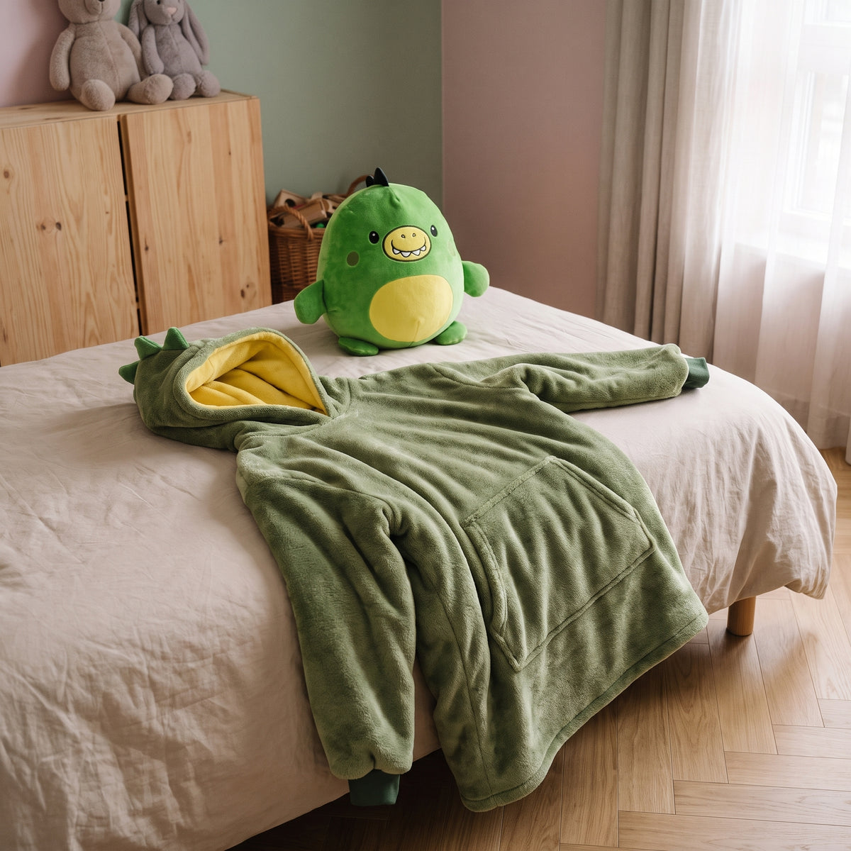 Plaid à capuche enfant dinosaure vert, posé au pied du lit avec son doudou