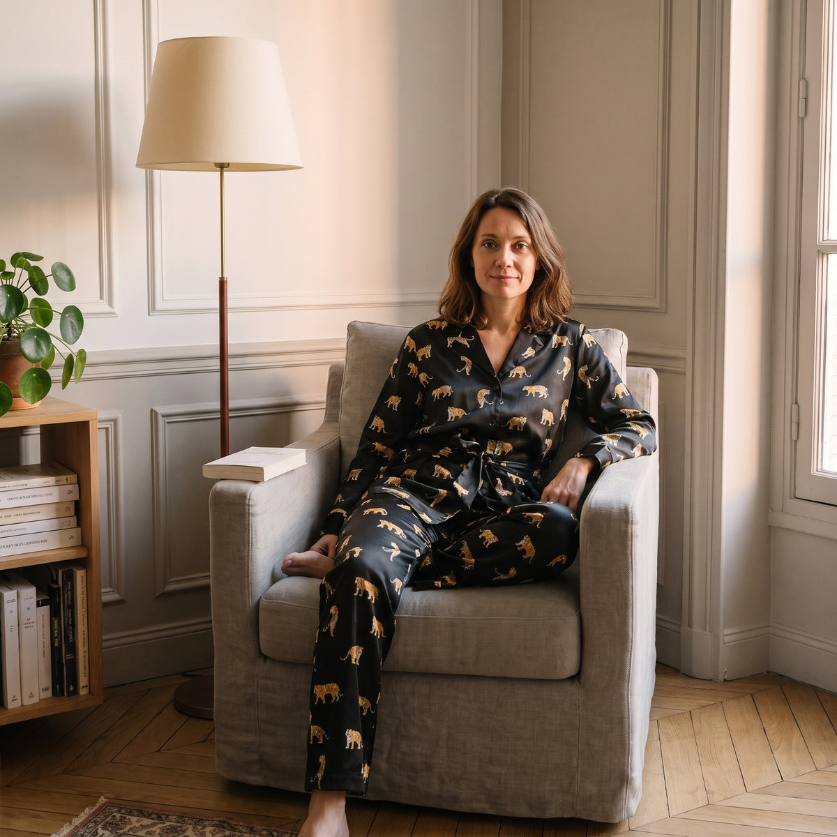 Femme assise dans un fauteuil de lecture en pyjama de satin imprimé tigres