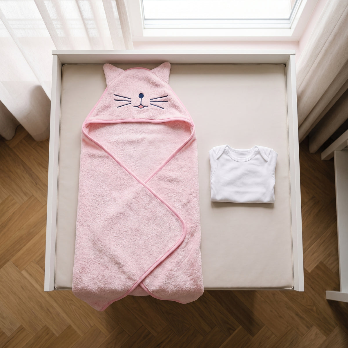 Cape de bain bebe depliee sur le matelas a langer a cote d un body de naissance