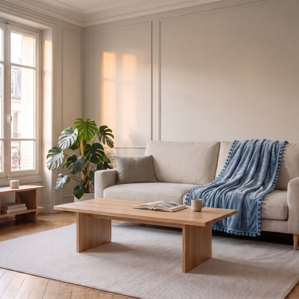 Plaid molletonné bleu gris à pompons posé sur une assise de canapé écru