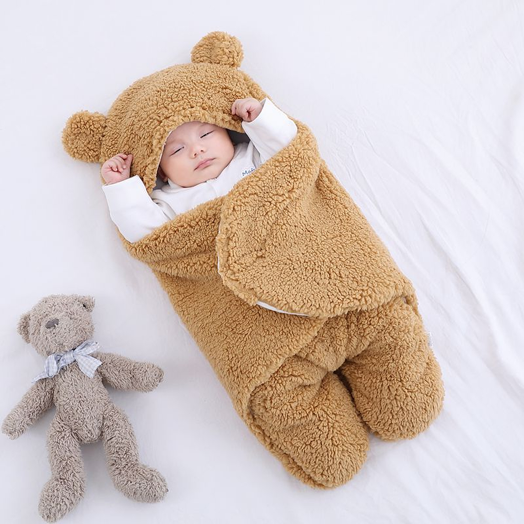 Bebe endormi dans la gigoteuse marron caramel, capuche relevee a oreilles, deux oursons en peluche poses a cote