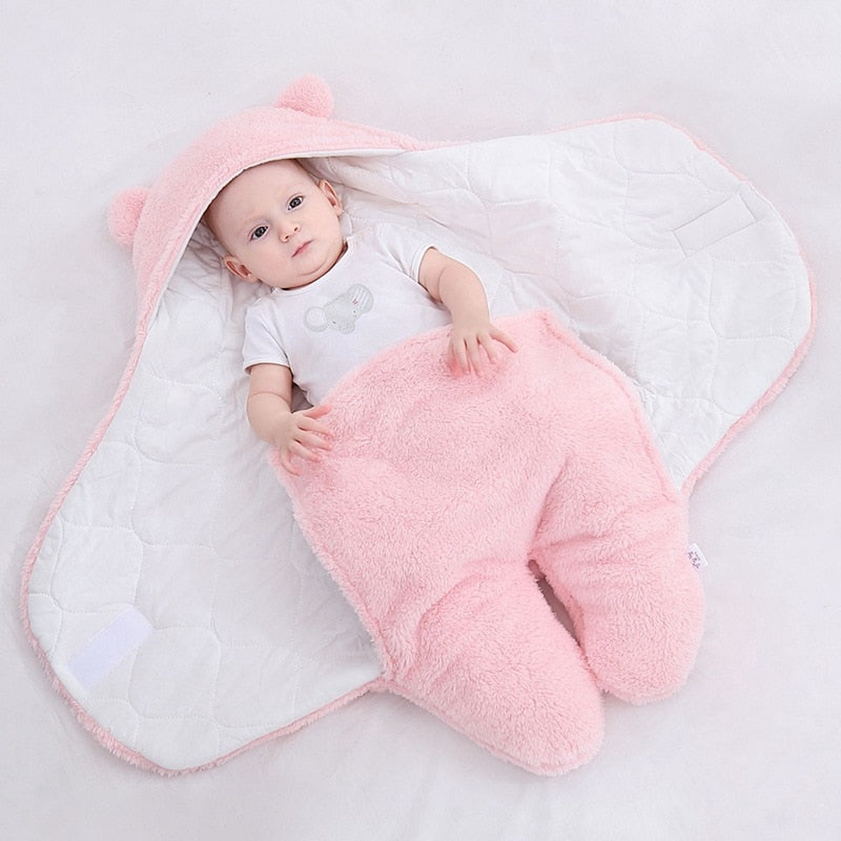 La gigoteuse rose ouverte a plat, un bebe couche au milieu : la doublure en coton matelasse blanc occupe tout l interieur, la bordure rose suit le contour et la capuche a oreilles est deployee en haut