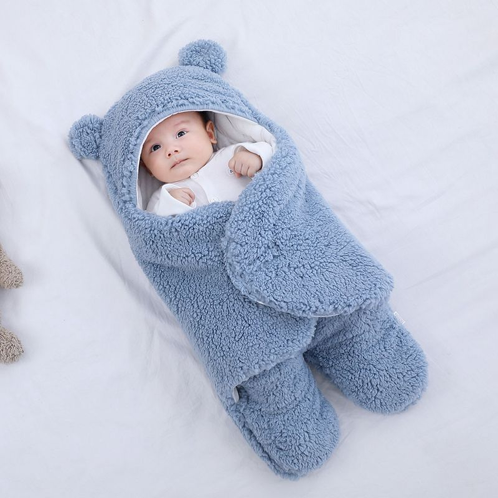 Bebe dans la gigoteuse bleue vue du dessus, pans croises sur le buste, capuche rejetee derriere la nuque et deux poches de jambes en bas