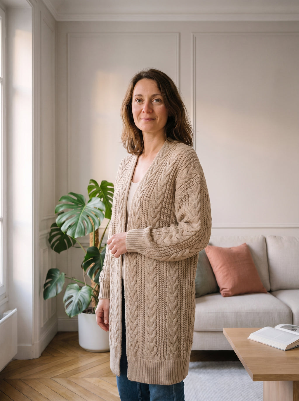 Femme du casting portant le gilet beige à grosses mailles dans le salon