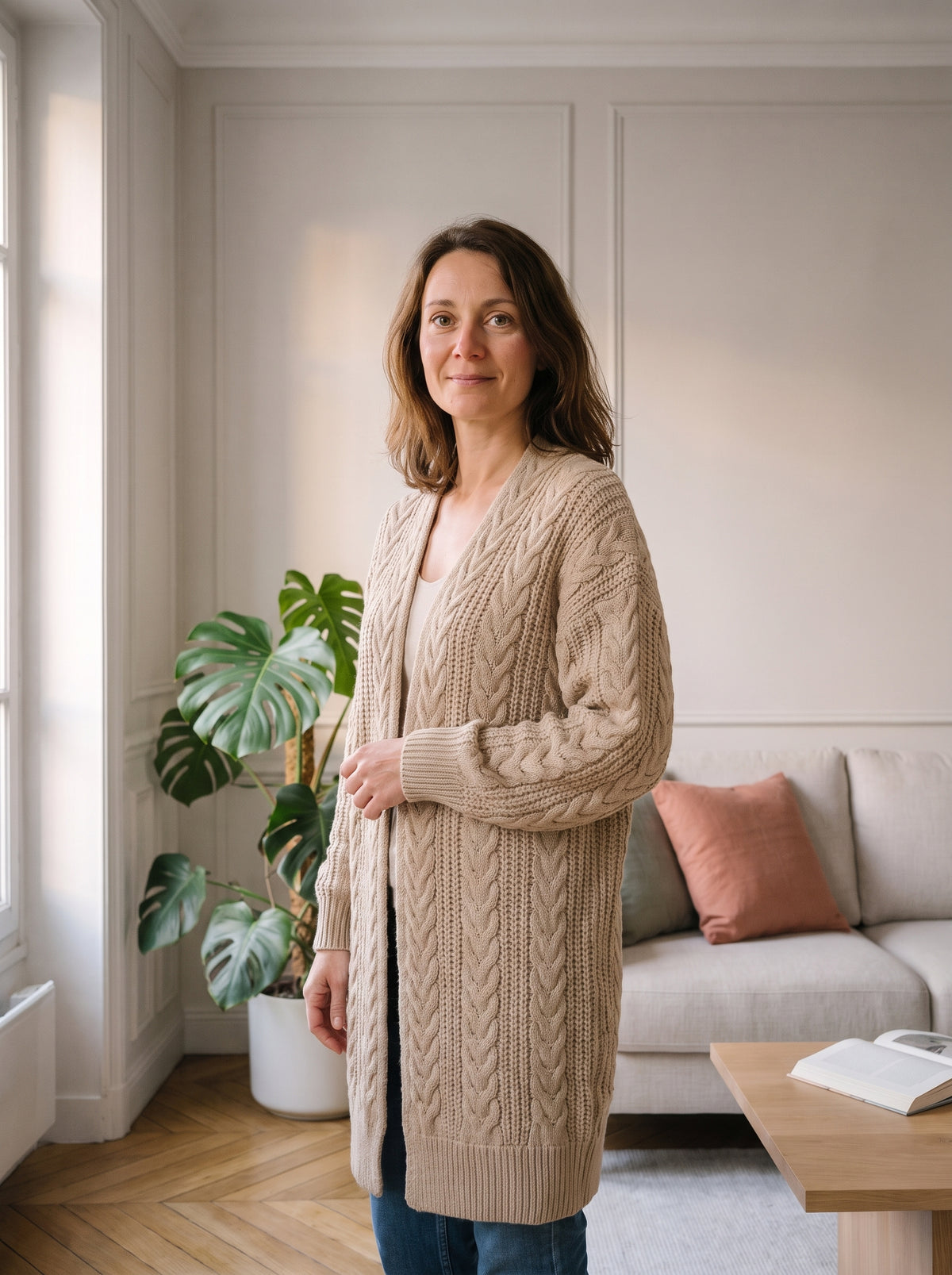 Femme du casting portant le gilet beige à grosses mailles dans le salon