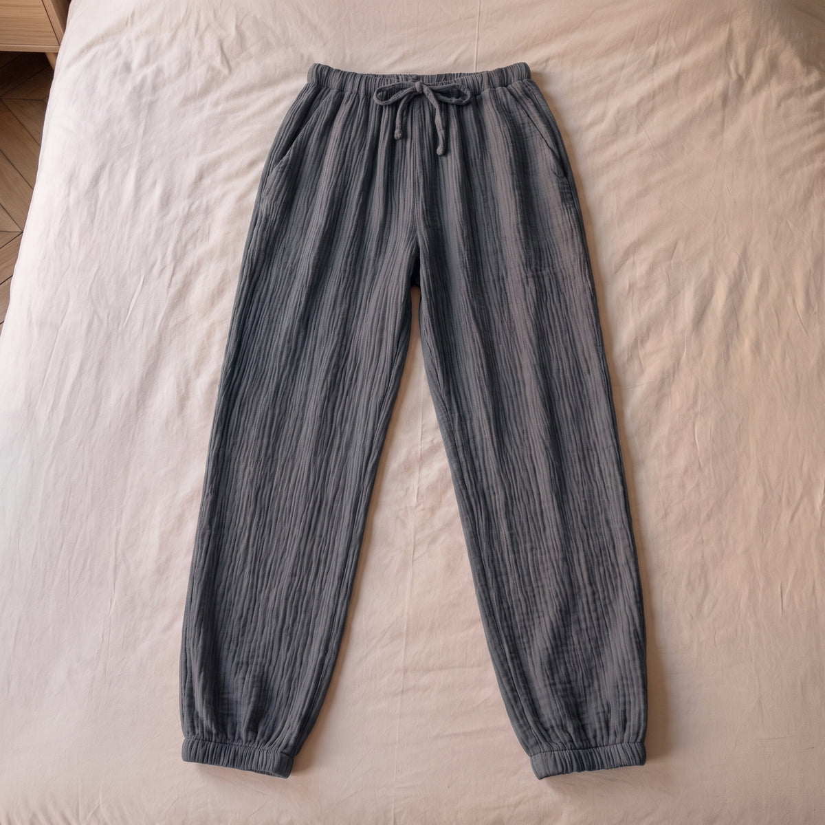 Pantalon de pyjama gris ardoise en gaze de coton pose a plat sur la literie, vu du dessus
