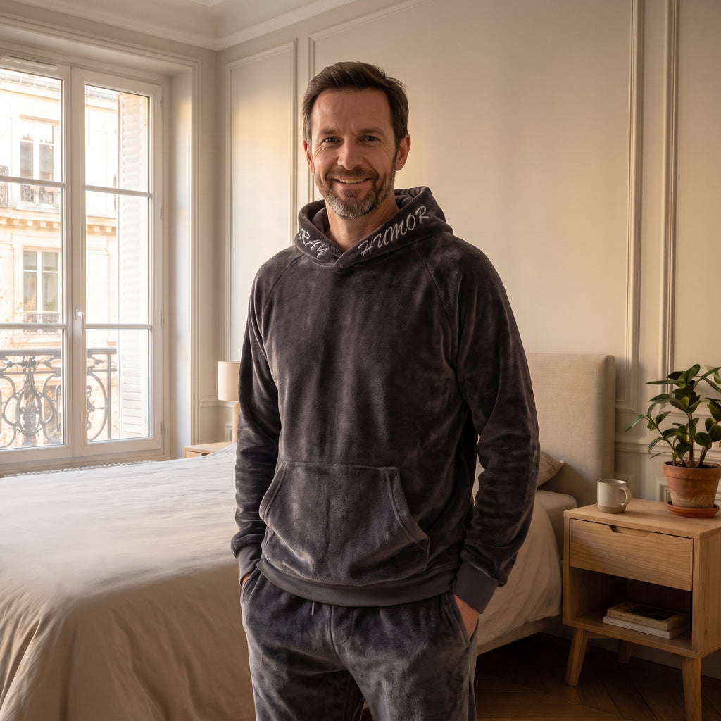 Pyjama polaire gris à capuche porté par un homme debout, les mains dans la poche ventrale, dans une chambre