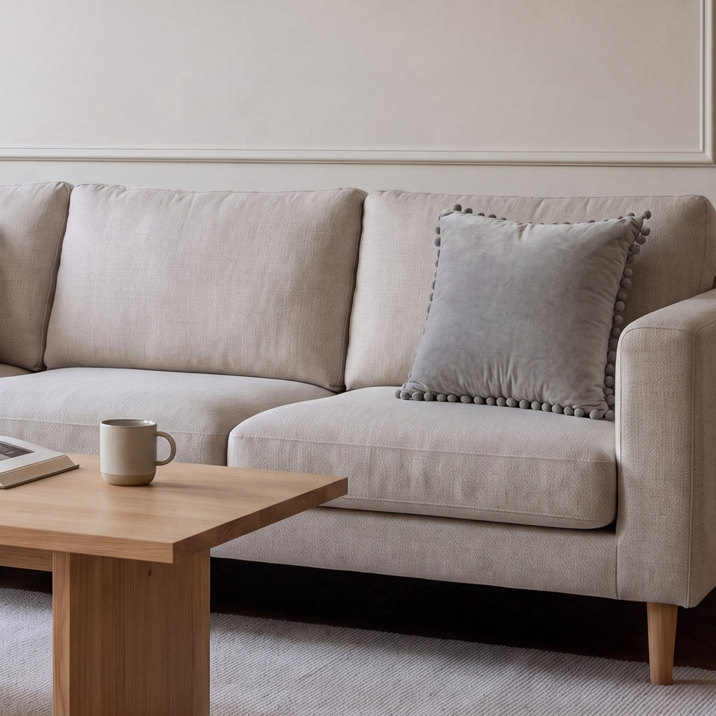 Housse de coussin en velours gris à pompons posée sur un canapé écru