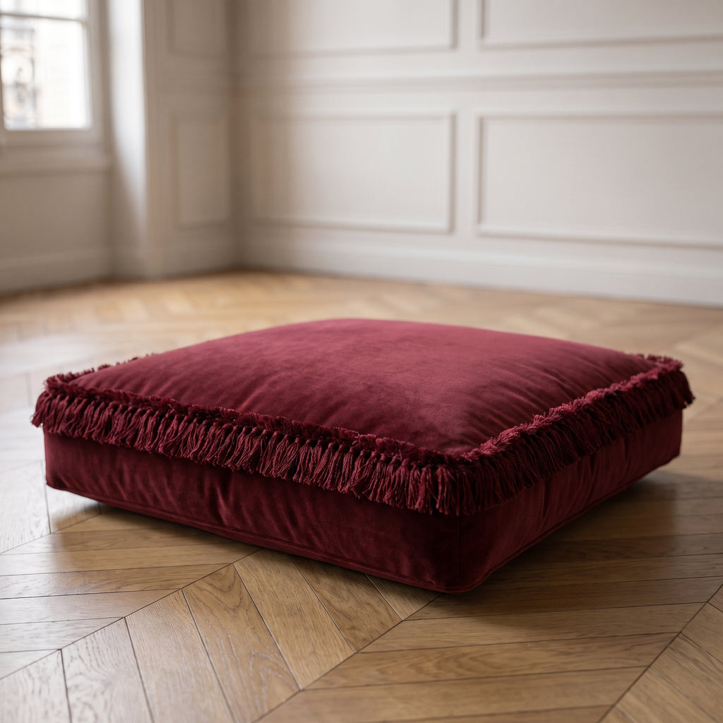 Coussin de sol en velours bordeaux à franges, posé sur un parquet