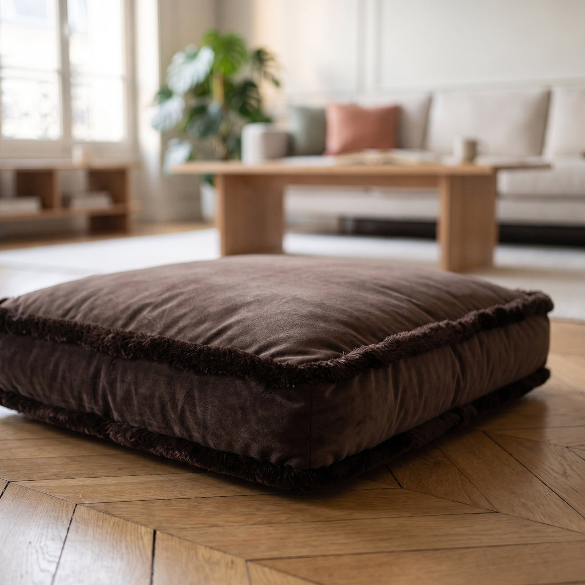 Coussin de sol en velours chocolat à franges, posé sur un parquet