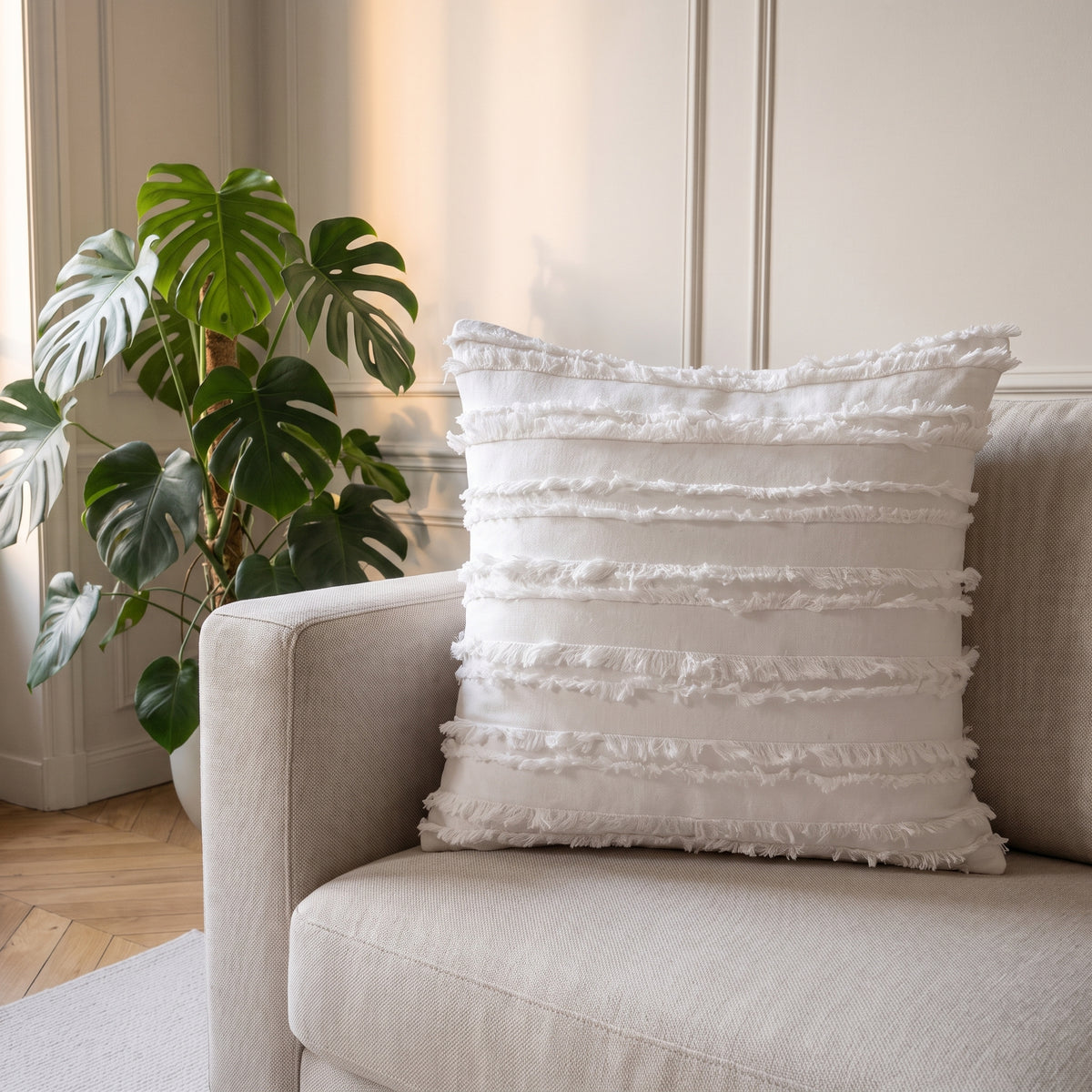 Housse de coussin bohème blanche à franges horizontales sur un canapé clair