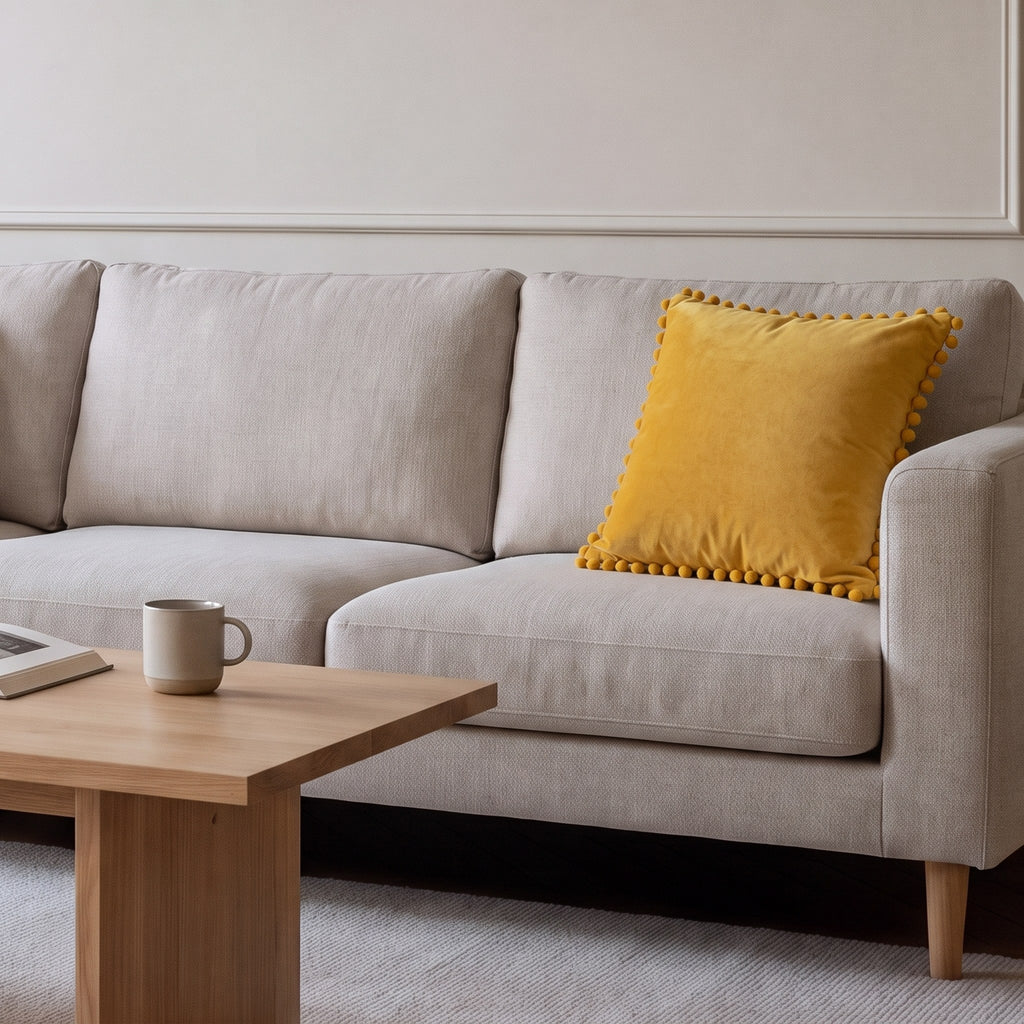 Housse de coussin en velours jaune à pompons posée sur un canapé écru