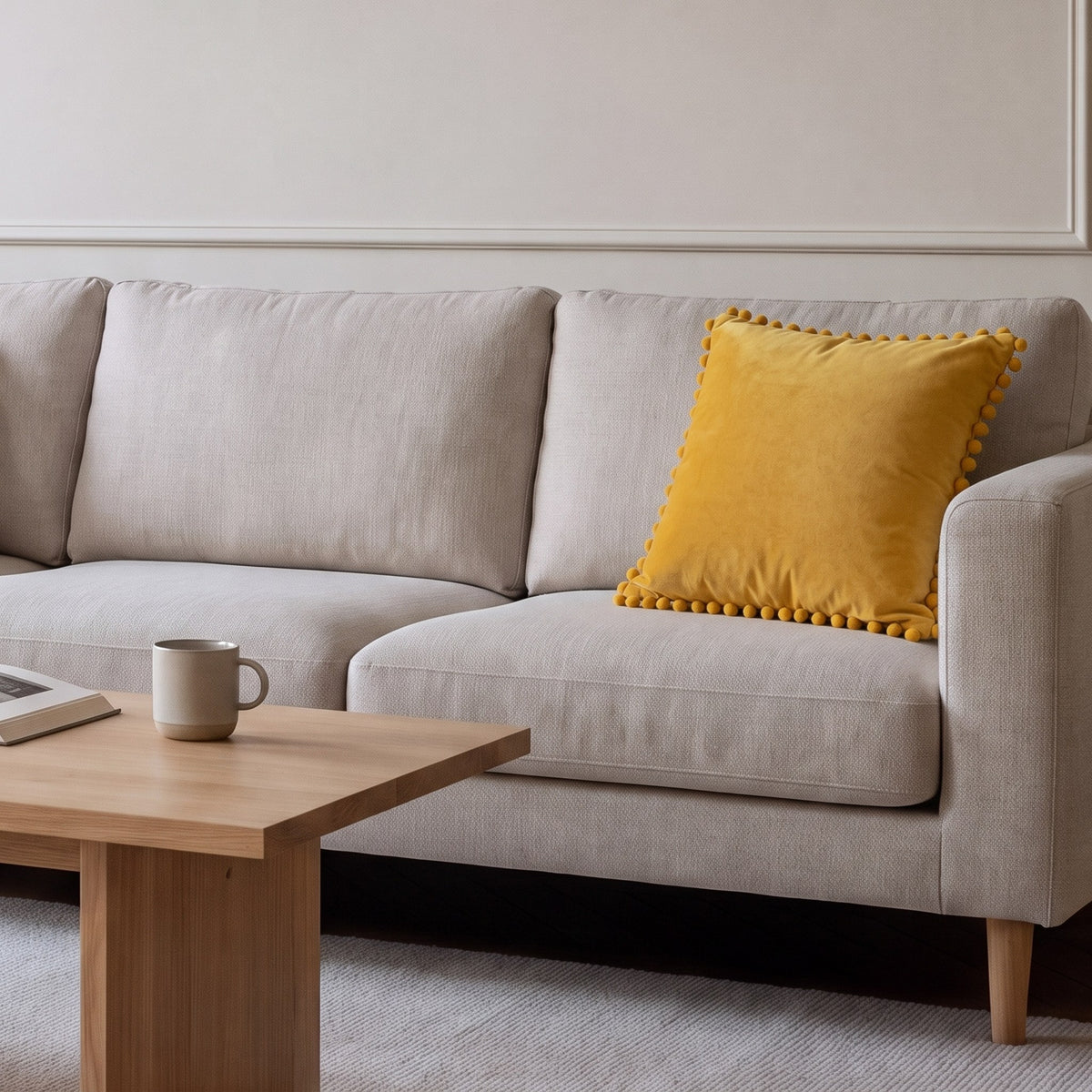 Housse de coussin en velours jaune à pompons posée sur un canapé écru