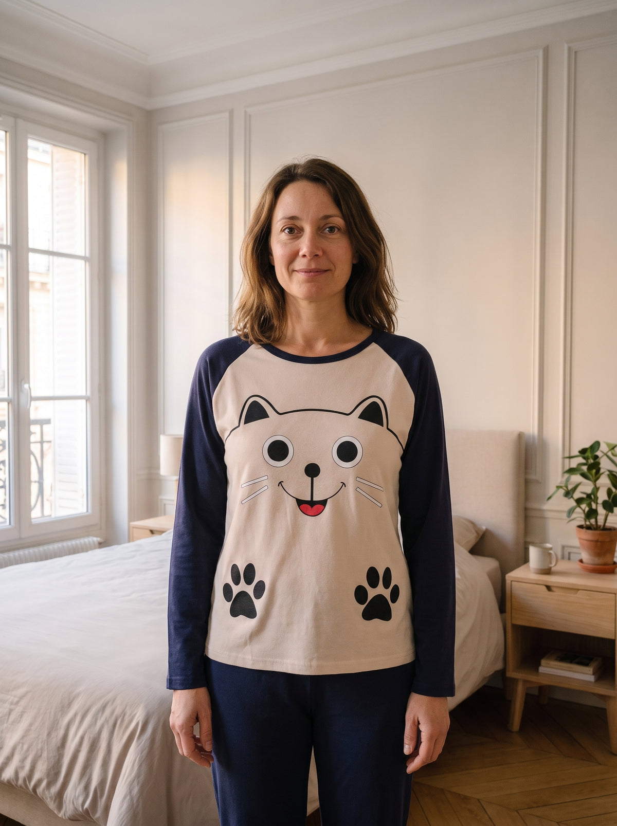 Femme du casting portant le pyjama chat beige et bleu marine dans une chambre lumineuse.
