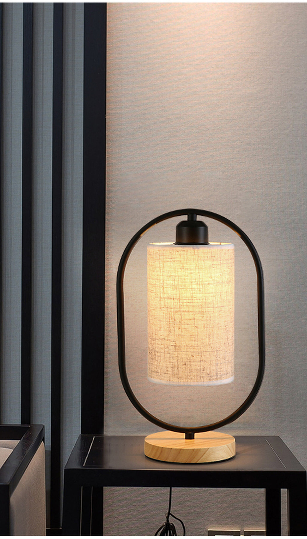 Lampe de chevet noire allumée sur une table, avec son cordon visible sous le plateau