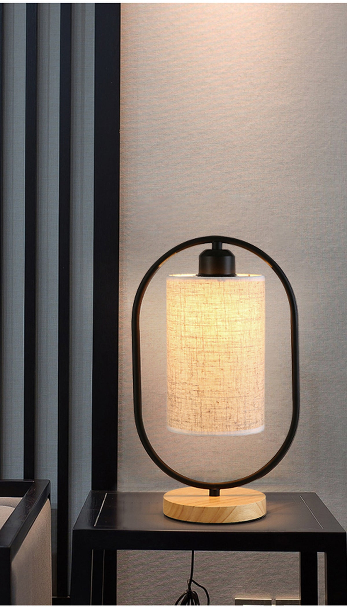 Lampe de chevet noire allumée sur une table, avec son cordon visible sous le plateau