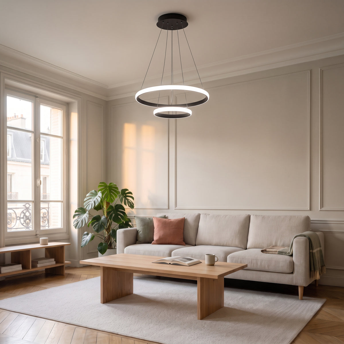 Plafonnier LED suspendu noir à deux anneaux au centre d’un salon aux tons naturels