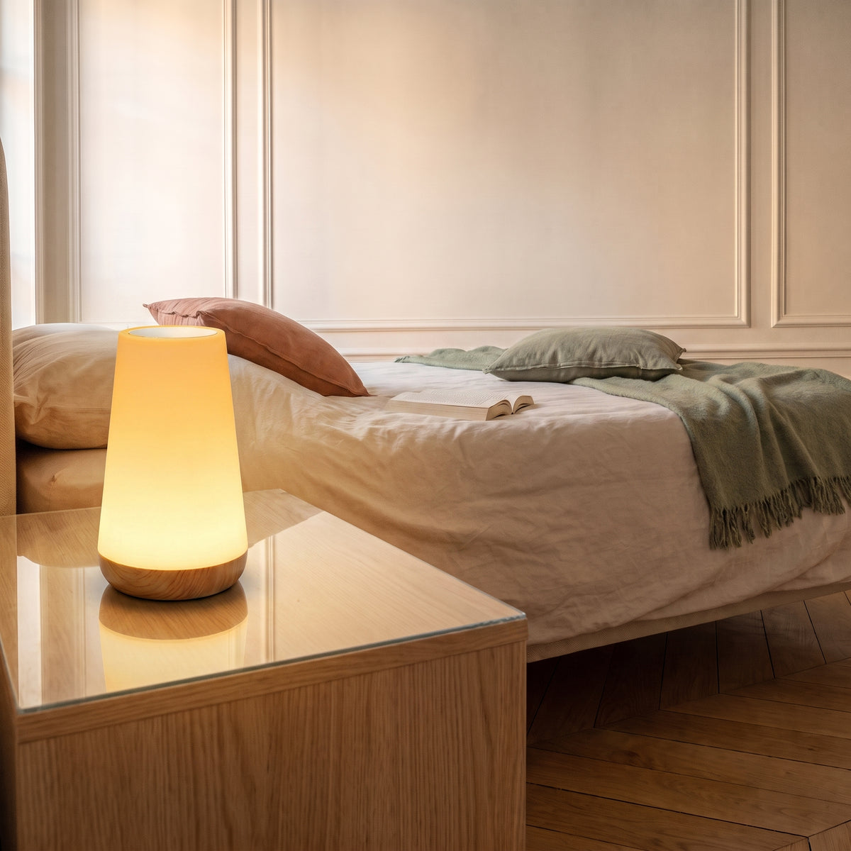 Lampe de chevet tactile allumée en lumière chaude sur une table de nuit en bois clair