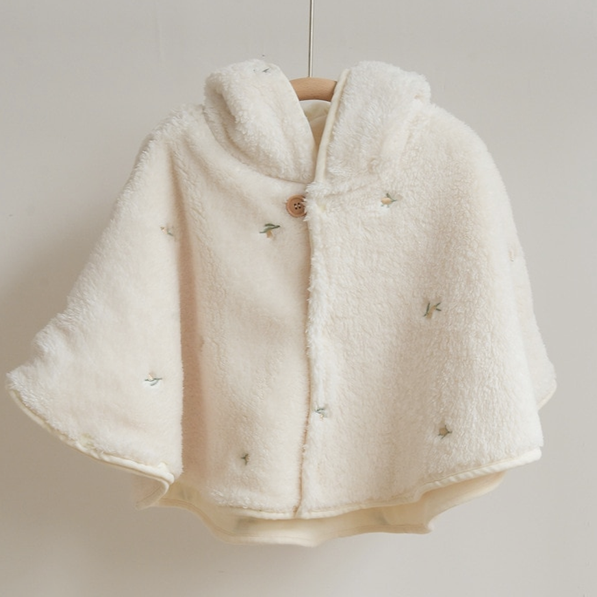 La cape motif petites fleurs a tige verte suspendue de face, bouton de bois au creux du cou