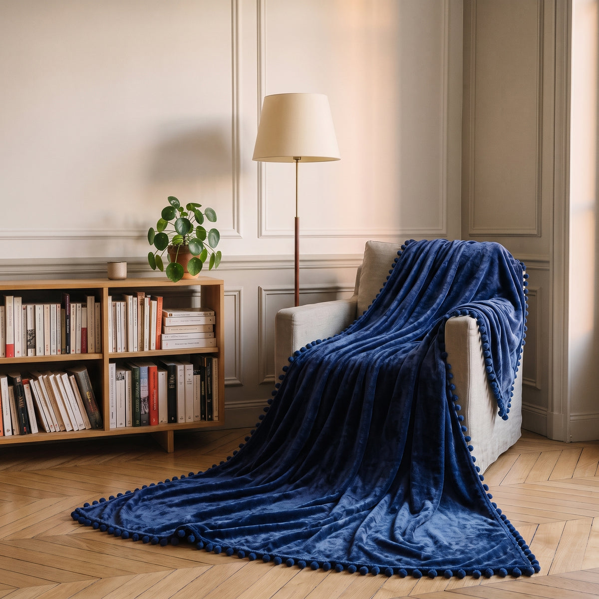 Plaid molletonné bleu marine à pompons posé sur un fauteuil de lecture