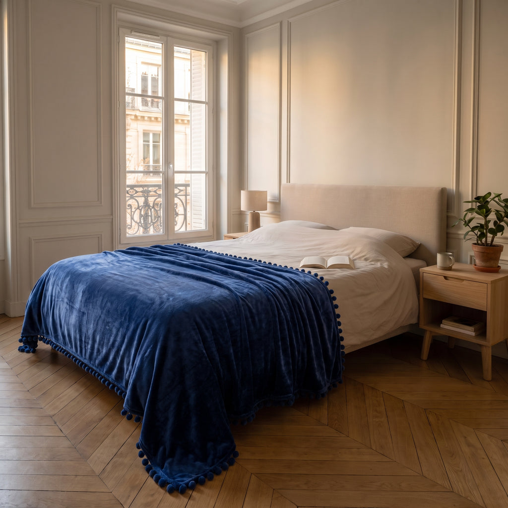 Plaid molletonné bleu marine à pompons déplié sur un lit deux places