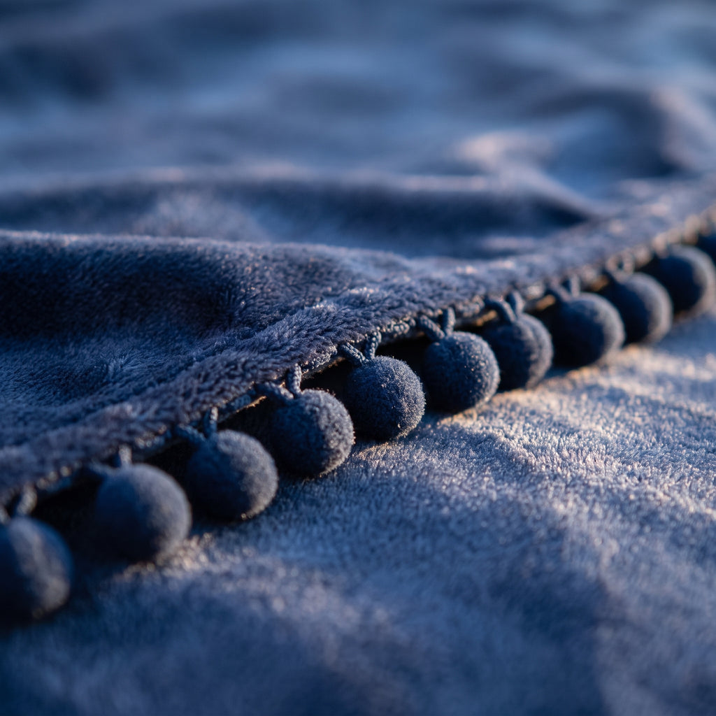 Détail de la bordure de pompons du plaid molletonné bleu marine à pompons