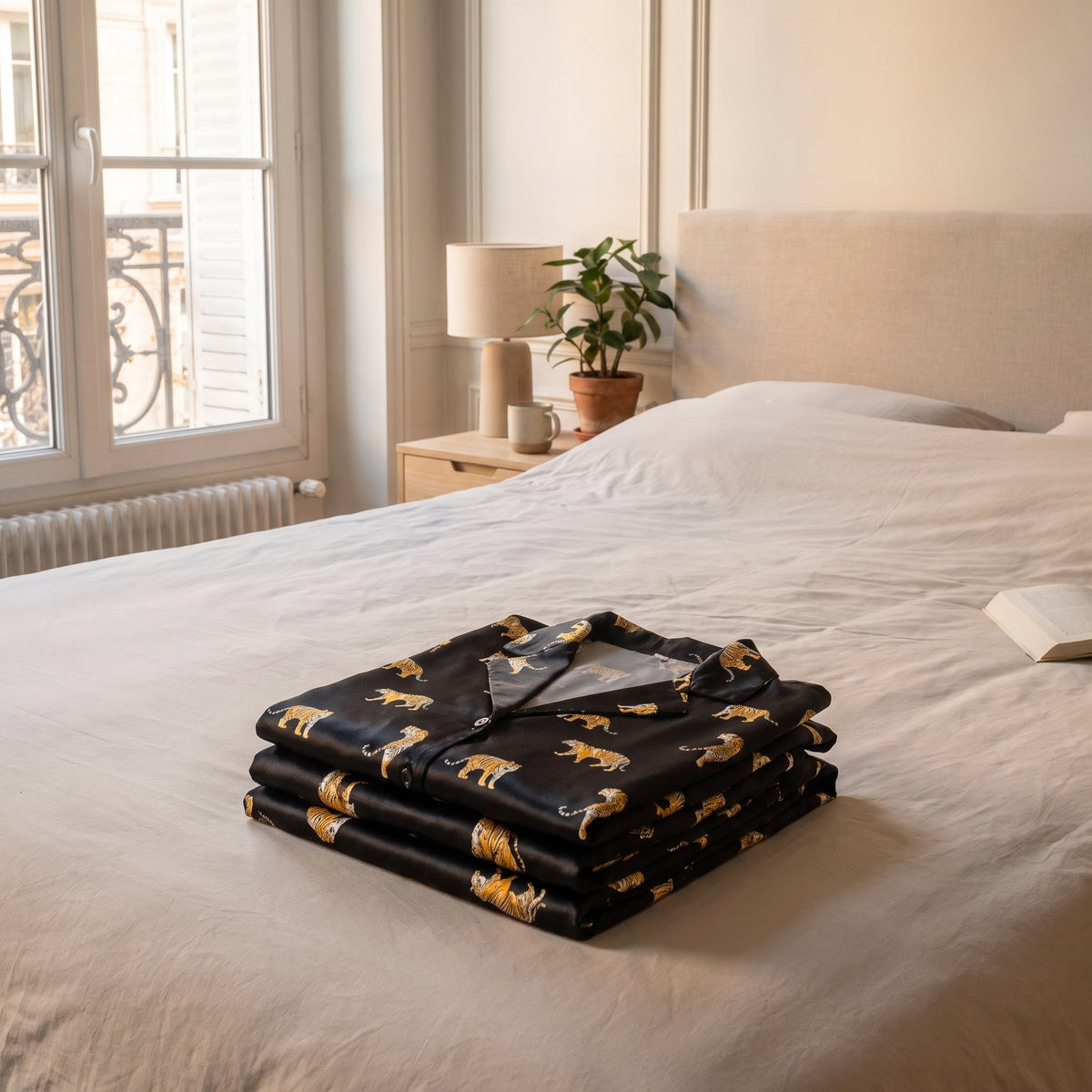 Pyjama en satin imprimé tigres plié en pile nette sur un couvre-lit Image