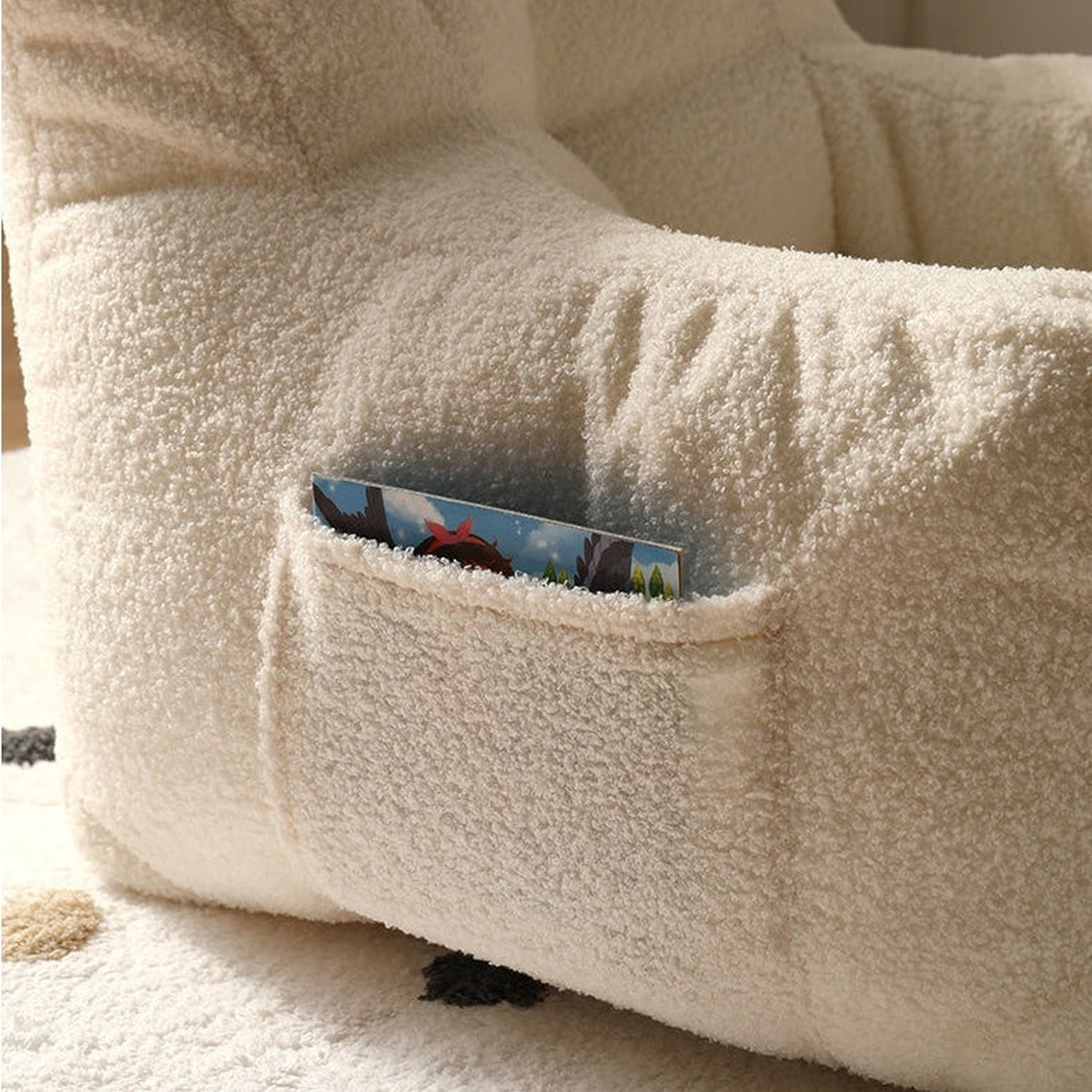 Poche latérale et surface bouclée du fauteuil enfant beige avec un album rangé Image