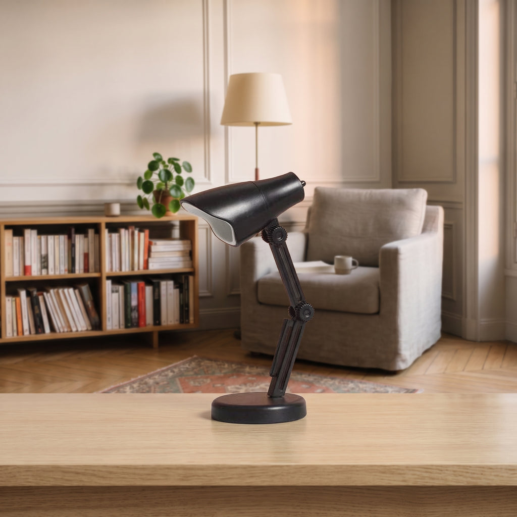 Mini lampe de lecture noire à abat-jour facetté posée sur un plan de travail en bois clair, vue de trois quarts