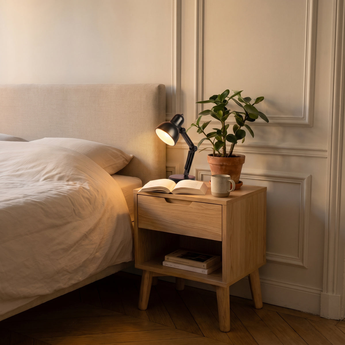 Mini lampe de lecture noire allumée sur une table de chevet en bois clair, éclairant un livre ouvert, le soir dans une chambre calme