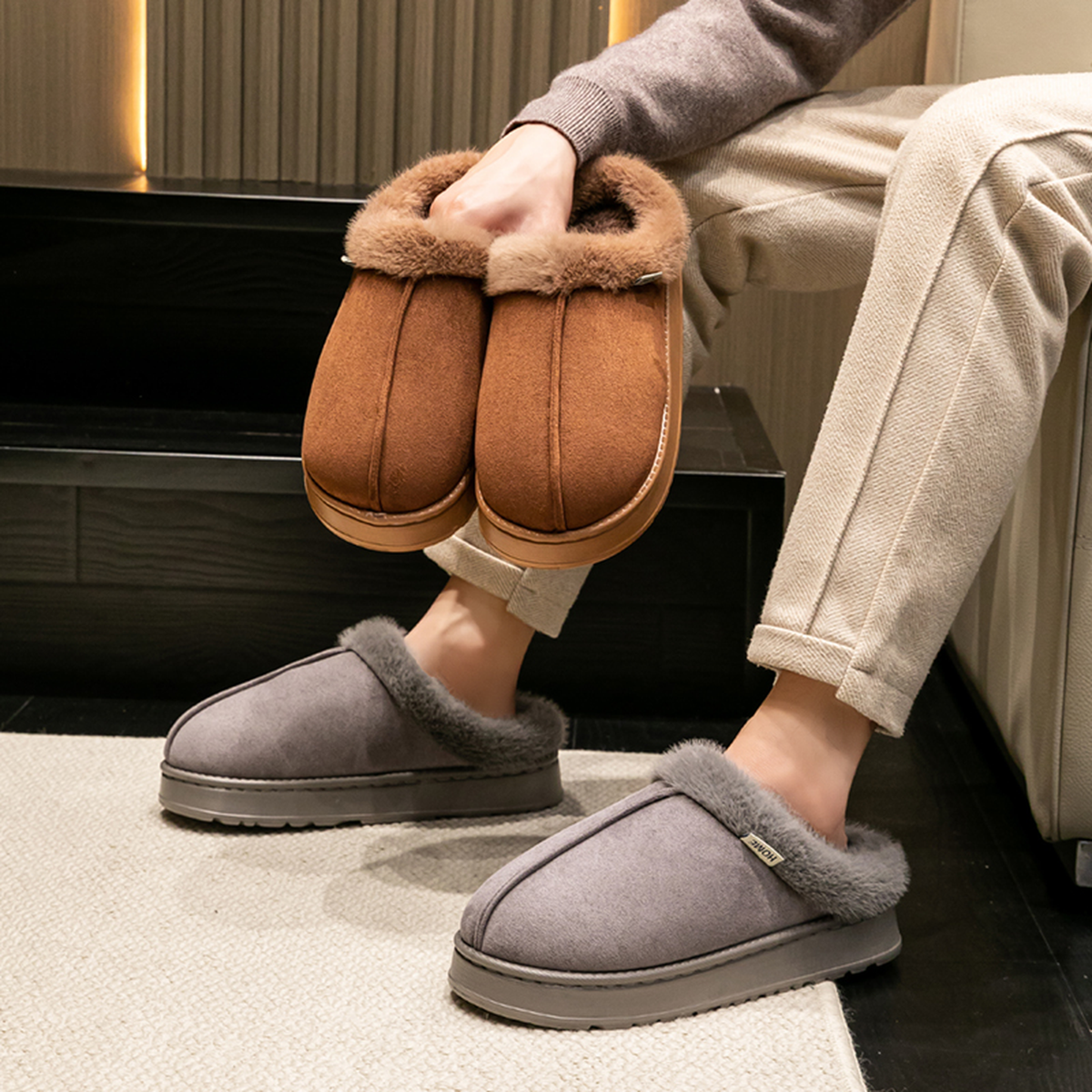Mules fourrées homme portées aux pieds, vues en Gris avec la paire Café en main