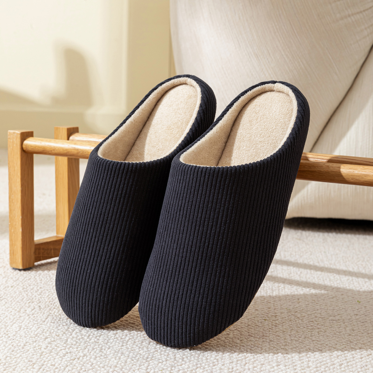 Paire de chaussons homme noirs en velours côtelé posée dans un salon chaleureux