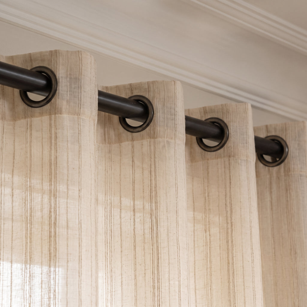 Tête du rideau beige à rayures brodées avec œillets enfilés sur la tringle