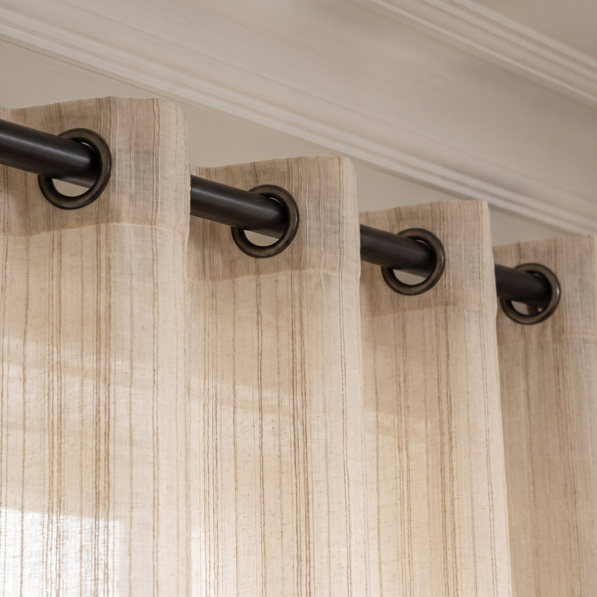 Tête du rideau beige à rayures brodées avec œillets enfilés sur la tringle