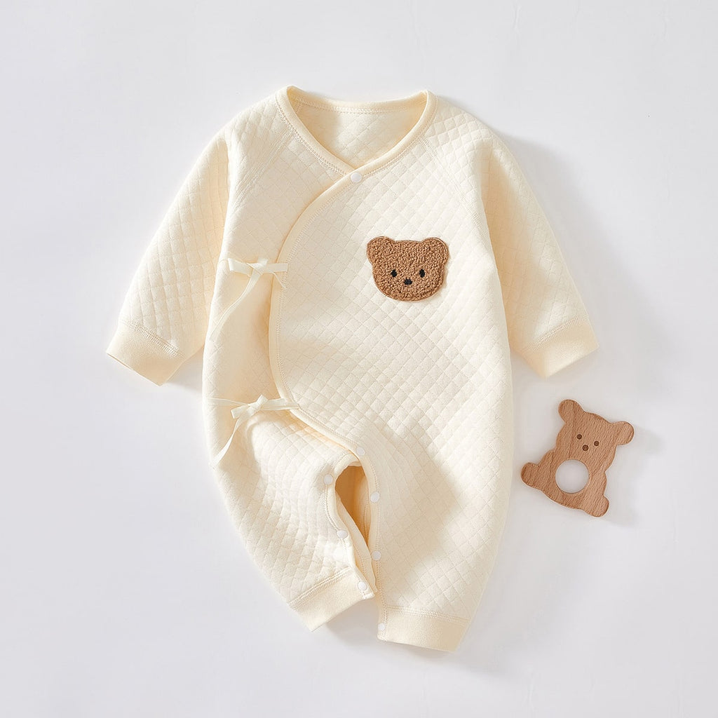 Barboteuse cache-coeur beige molletonnée avec une tête d'ours en peluche dessus et un hochet ourson à côté